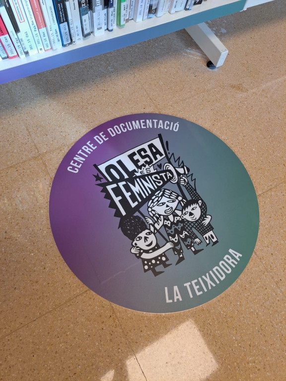 Logotip del SIAD D'Olesa - La Teixidora davant la prestatgeria de color lila del nou catàleg