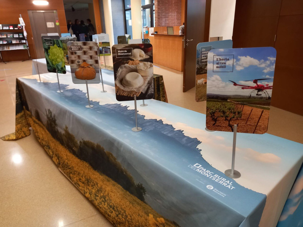 Exposició sobre una taula amb una gran fotografia de les muntanyes de Montserrat i a sobre cartells amb productes propis