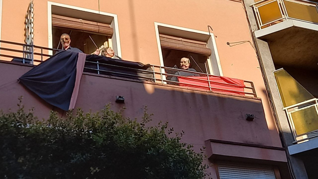 Tres persones a un balcó amb caretes fent perfomance