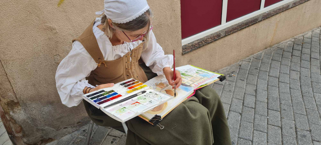 Dona caracteritzada sentada dibuixant i pintant